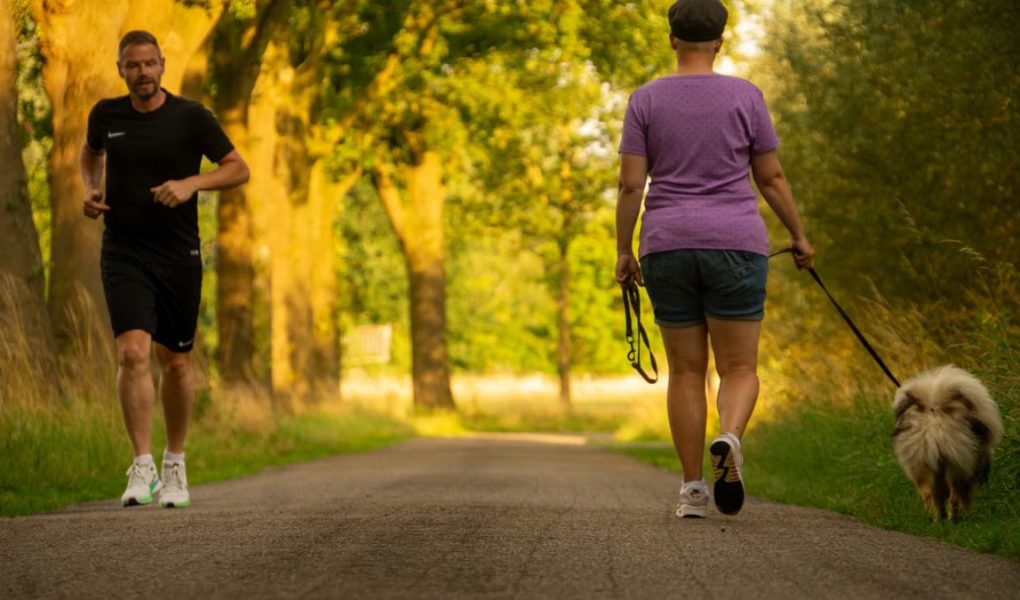 Man jogging and woman walking a dog on a picturesque outdoor path.