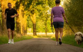 Man jogging and woman walking a dog on a picturesque outdoor path.