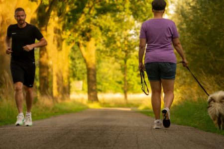 Man jogging and woman walking a dog on a picturesque outdoor path.