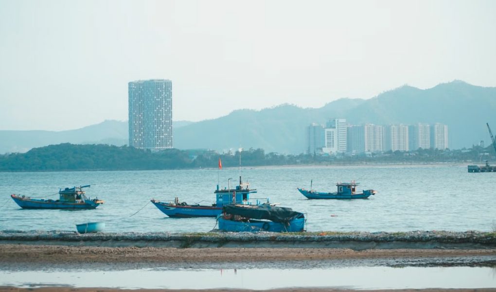 Scenic view of fishing boats in Da Nang harbor with urban skyline and mountains.