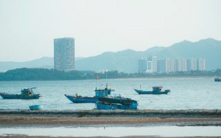 Scenic view of fishing boats in Da Nang harbor with urban skyline and mountains.